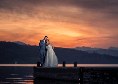 bride and groom on jetty at windermere sunset